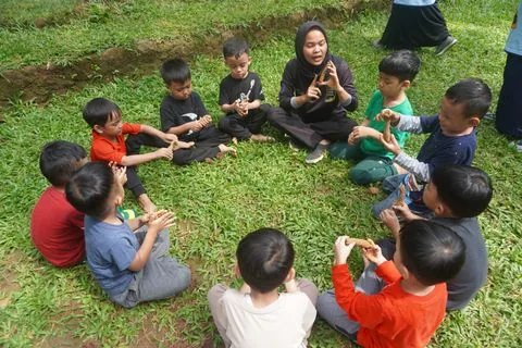 Murid TK duduk melingkar di rumput saat kegiatan luar ruang